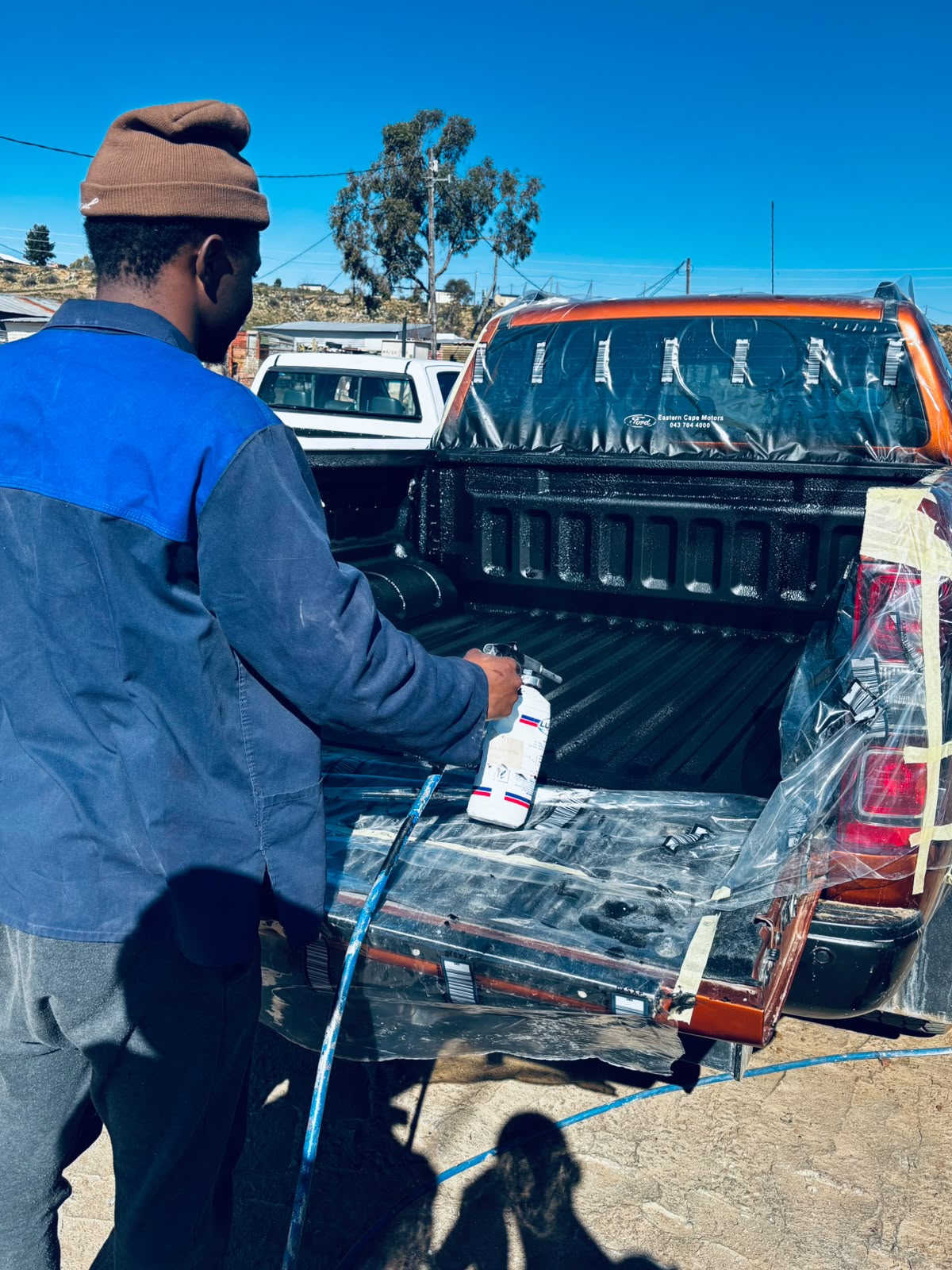 Technician spray painting a masked bakkie load bin